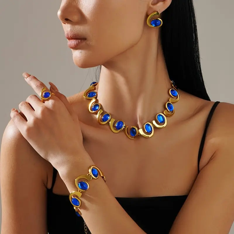 Um conjunto de quatro peças de joias femininas elegantes que destacam um bracelete, colar, anel e brincos em forma de espiral geométrica de acrílico azul, com tema de oceano. Este conjunto de joias metálicas é perfeito para férias na praia e festas.